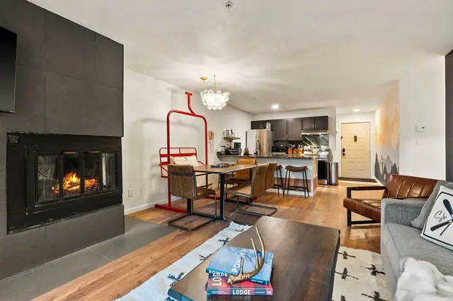 Grab a book off the coffee table stack and claim a seat by the fire — from here you can see the table set for dinner and the kitchen still going in the background.