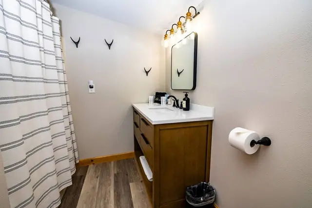 Get yourself ready at the wood vanity under warm sconce lighting, a subtle antler silhouette watching from the wall.