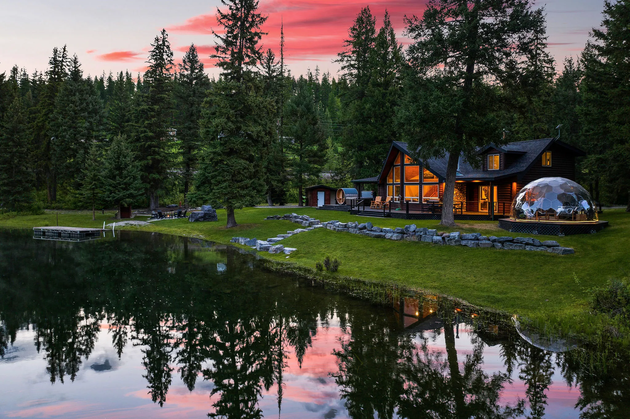 Lodge 93 across the river channel at sunset, the cabin and geodome glowing and the whole sky mirrored in the water