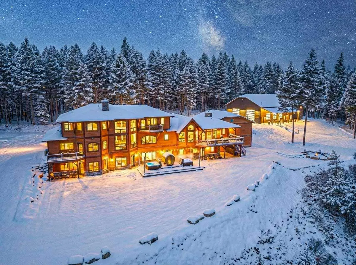 The Milky Way over snow-laden pines and the lit house below