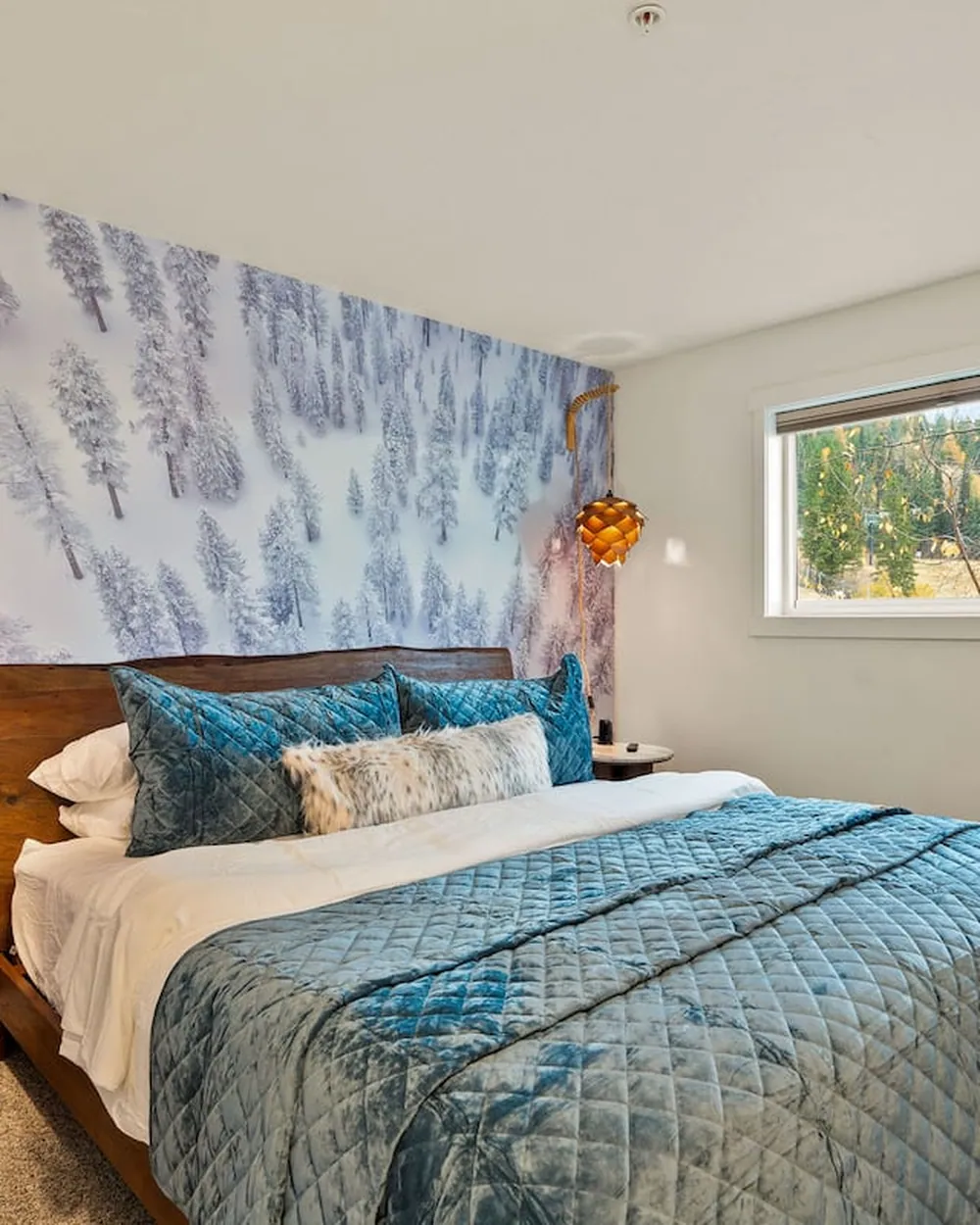 A bedroom at Chasing Powder, a wall of snow-laden pines behind the bed and the mountain framed in the window