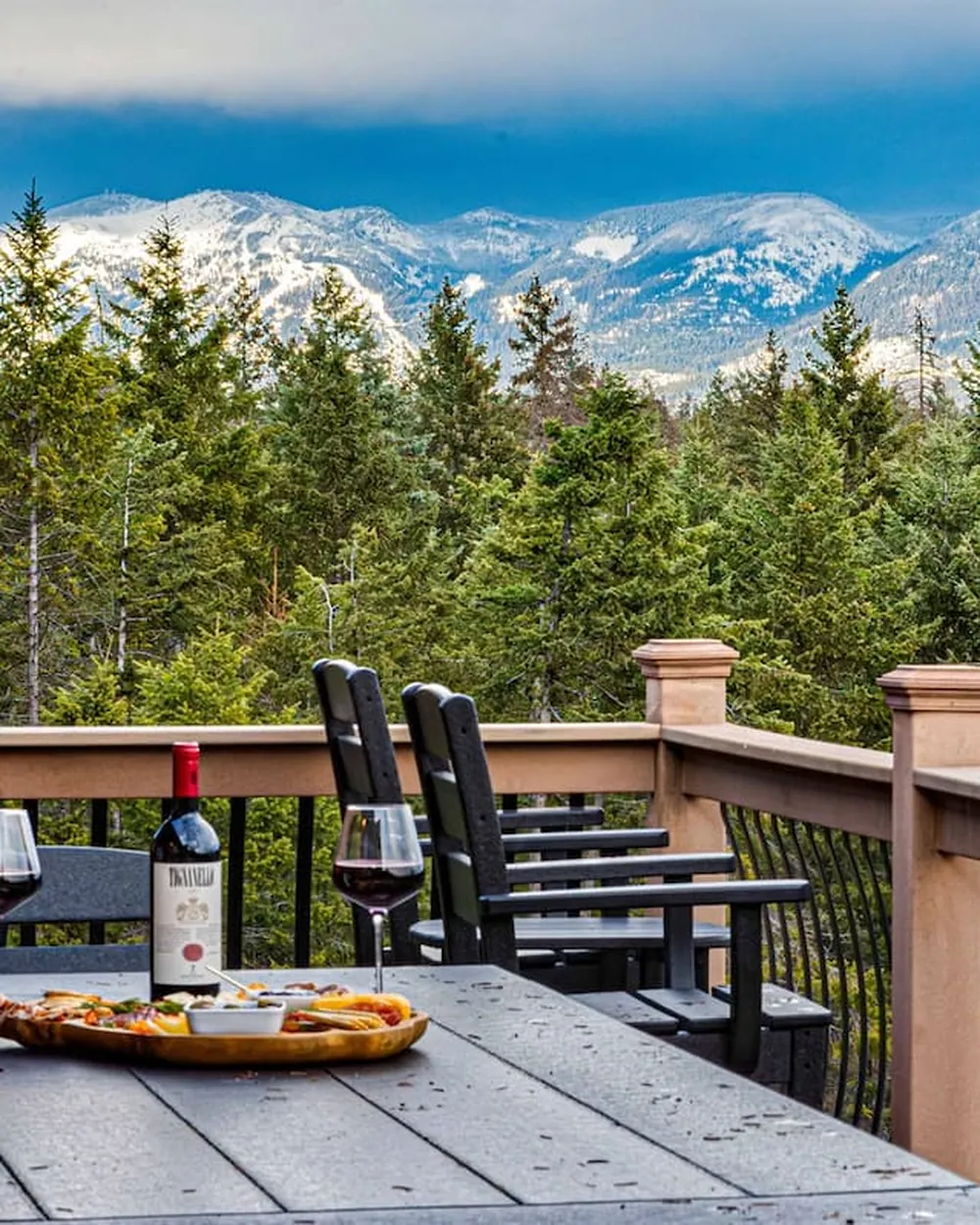 A long deck table set with wine and charcuterie above the treetops at Soaring Eagle, the range still holding snow