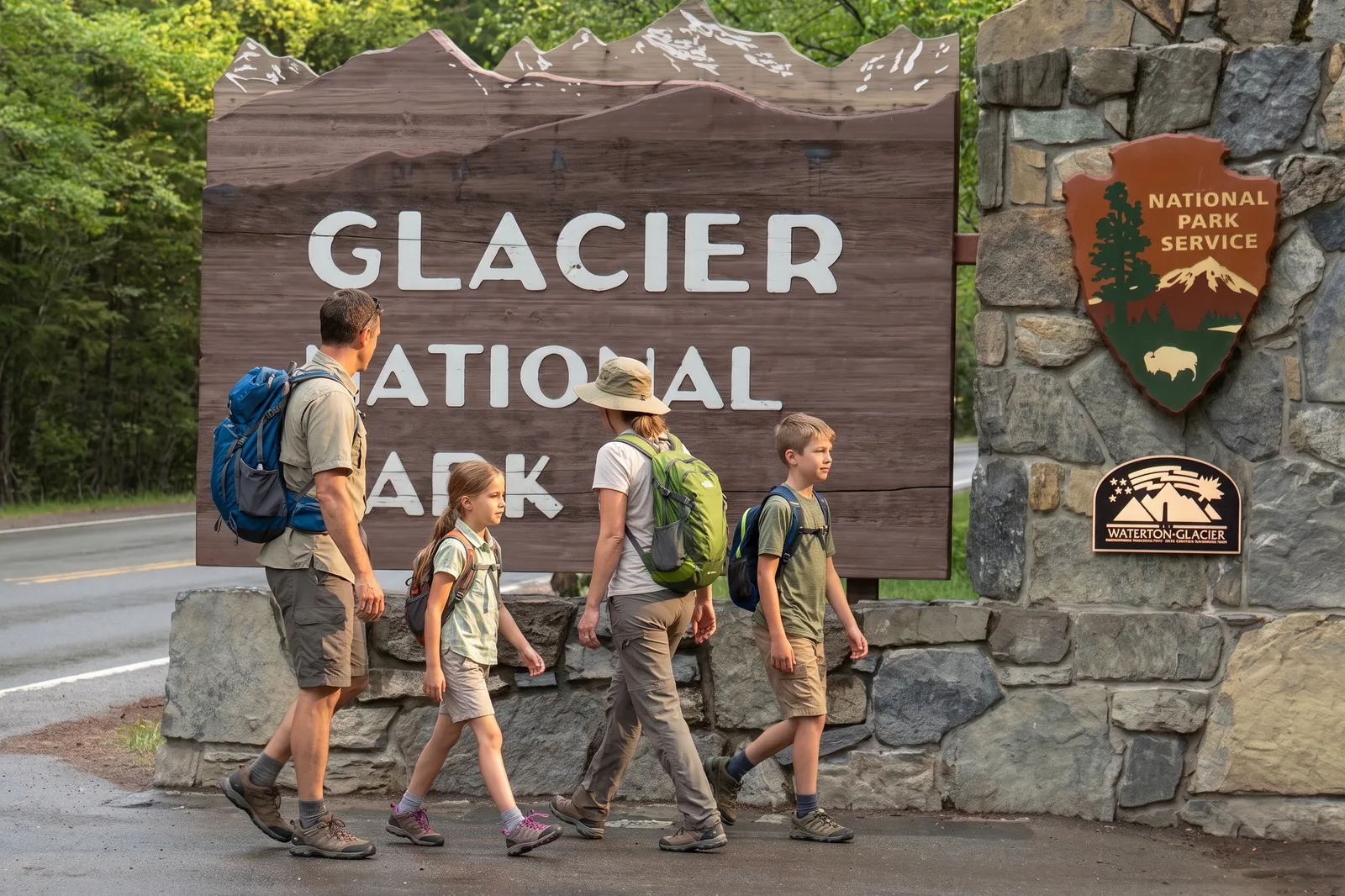 A family with daypacks walking past the Glacier National Park entrance sign, minutes from Glacier Getaway