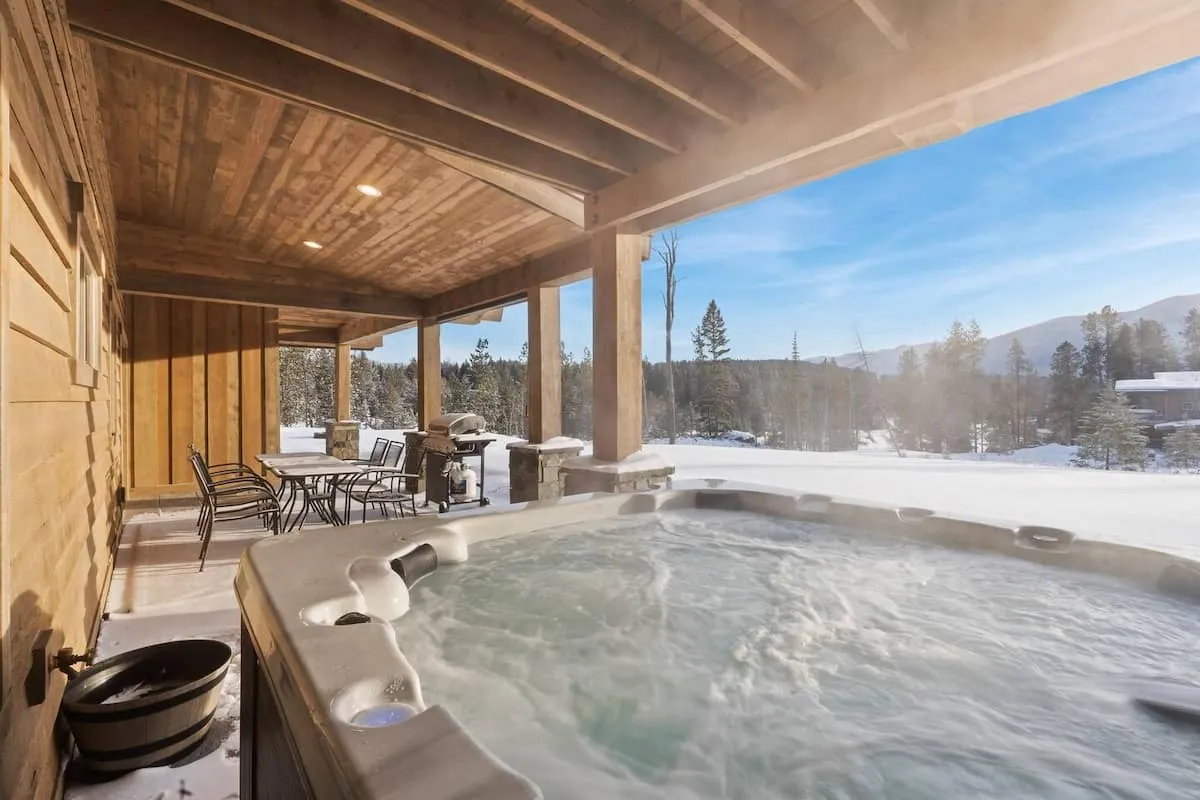 Hot tub steaming on a covered patio against snow-capped peaks