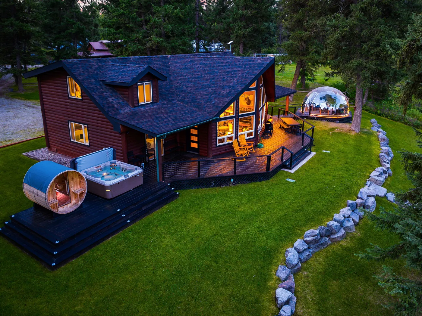 Lodge 93 at dusk with its hot tub, barrel sauna and glowing geodome on the lawn