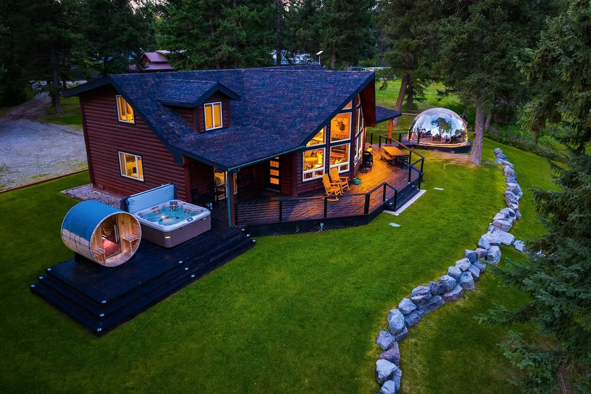 The cabin at dusk with its hot tub, barrel sauna and glowing geodome