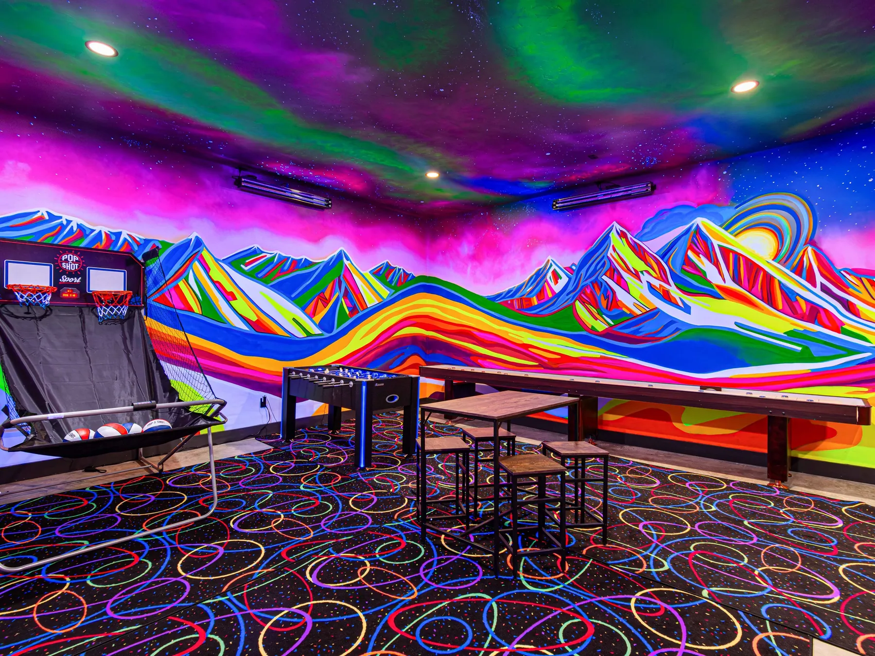 The black-light game room, its painted mountains glowing over the shuffleboard table