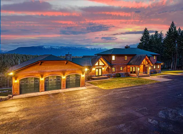 Arrive at twilight to warm lit windows, your three-car garage wing, and a pink sunset settling over the mountains.