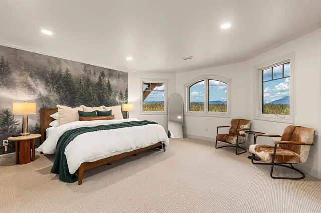 Rest under a wall-sized forest mural on the king bed, two fireside-style chairs positioned by the window for a mountain view.