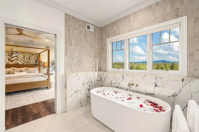 Sink into the petal-strewn water of the oval soaking tub with the canopy bedroom visible just through the doorway.