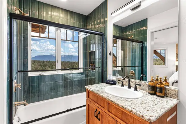 Shower with a mountain view through the window, gold-capped amenity bottles lined up at your vanity.
