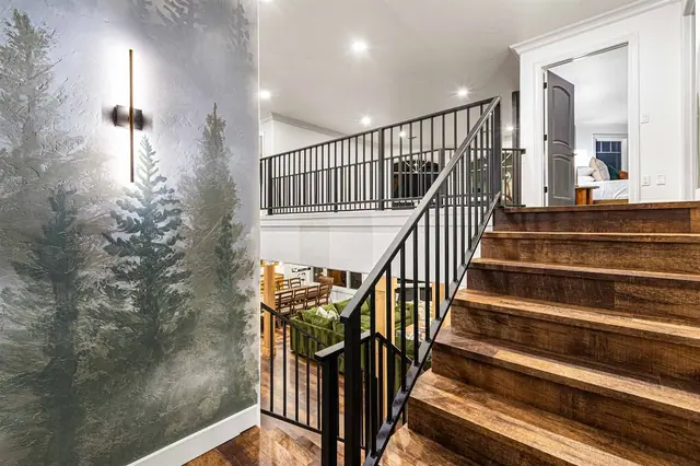 Climb the staircase past the lit sconce and forest mural, overlooking the furnished loft below.