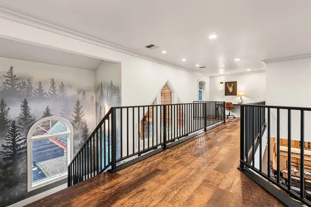 Post up at the loft desk overlooking the stairwell, snow visible through the arched window beside the forest mural.